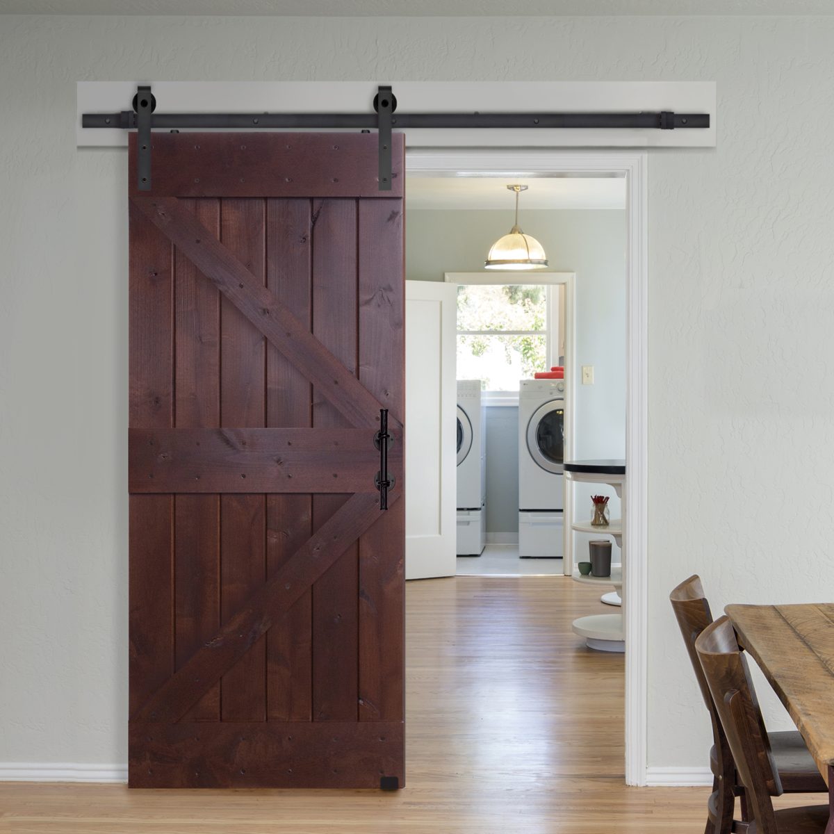 Dark stained Double Z barn door slid open on a black rail beside the doorway to a laundry room